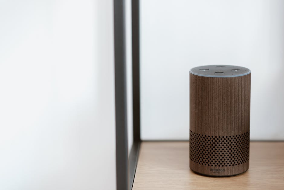 A sleek, modern smart speaker displayed on a wooden shelf in a minimalist room setting.