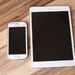 A white smartphone and tablet placed on a wooden table, showcasing technology contrast.