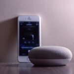 A modern smart speaker and smartphone on a wooden table, indoors.